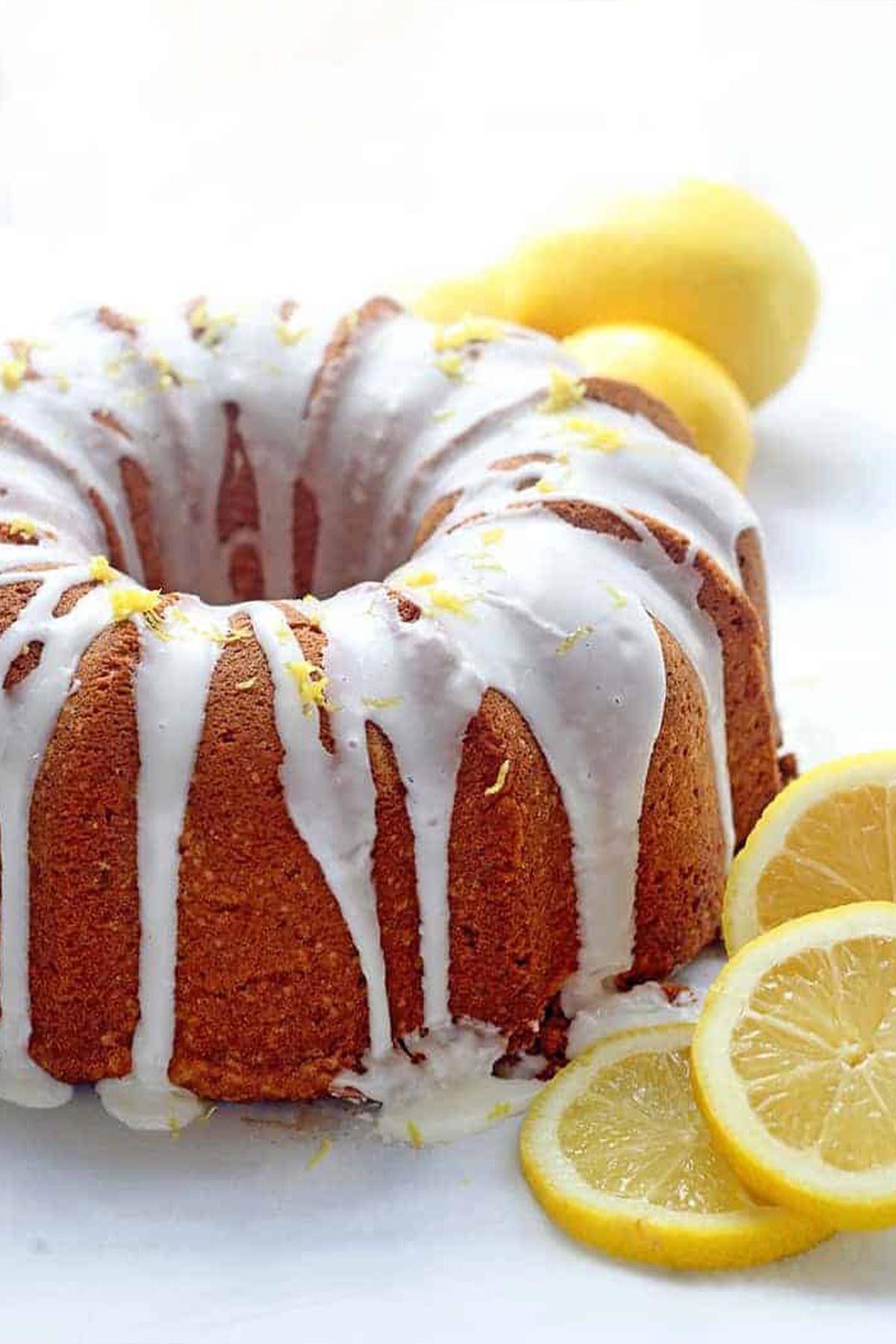 A lemon pound cake on the table with glaze and fresh slices of lemon.
