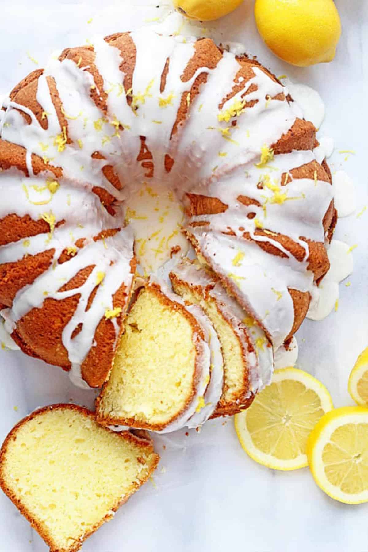 Overhead shot of the Lemon Pound Cake with slices cut out of it and whole lemons and lemon slices next to it. 