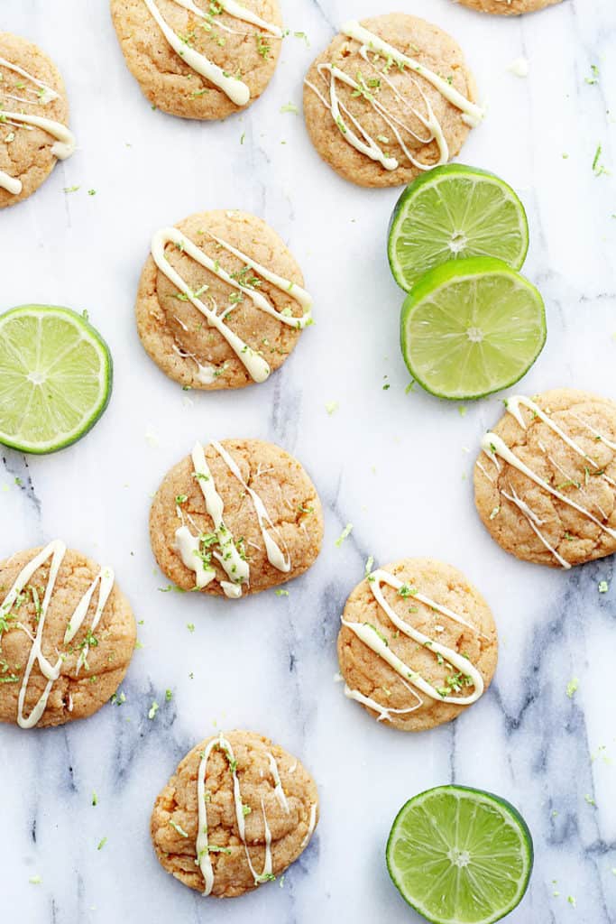 Overhead shot of several key lime pie cookies on a marble surface with key lime slices