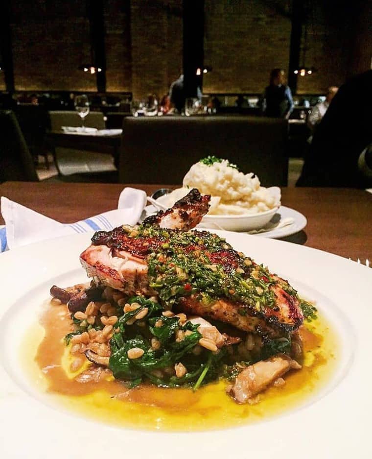 Amazing chicken dish on a white plate with a bowl of mashed potatoes in the background