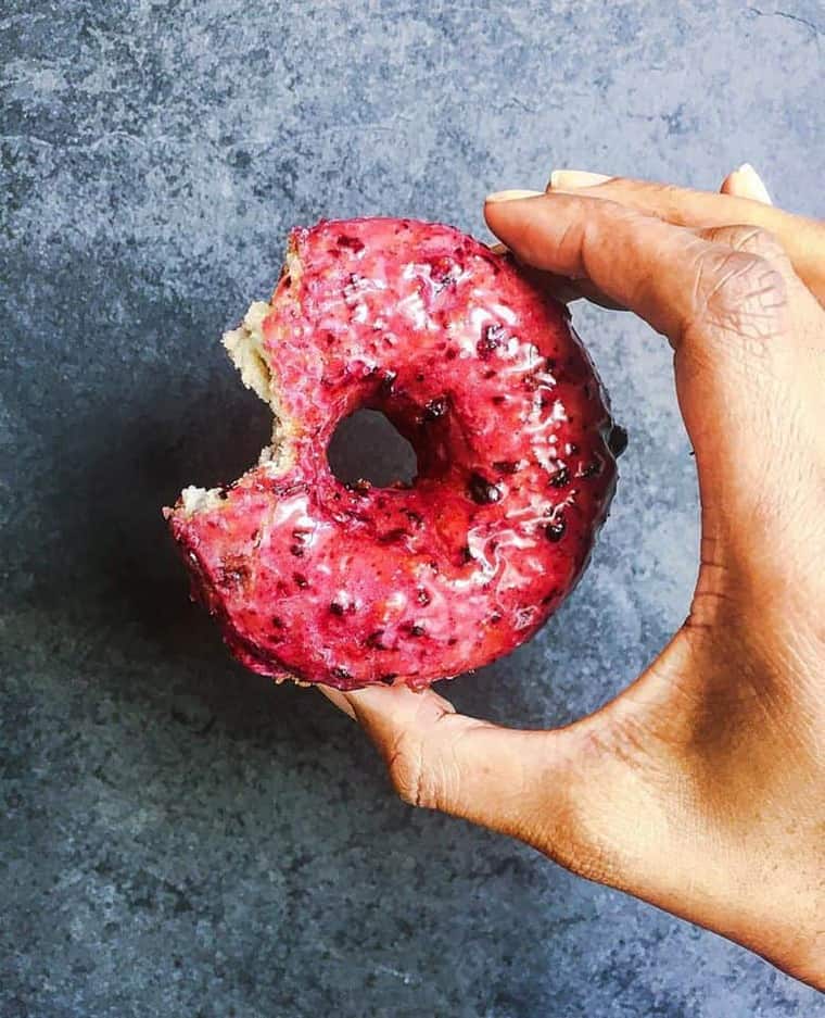 Half eaten donut being held against a blue background in L.A.