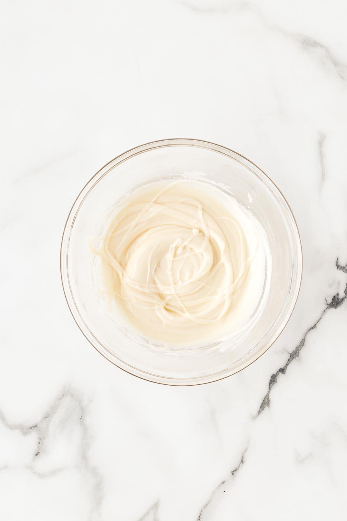 Glass bowl of smooth white chocolate glaze swirled and ready for drizzling