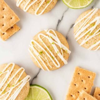 Overhead shot of key lime pie cookies drizzled with white chocolate glaze, surrounded by lime slices and graham crackers
