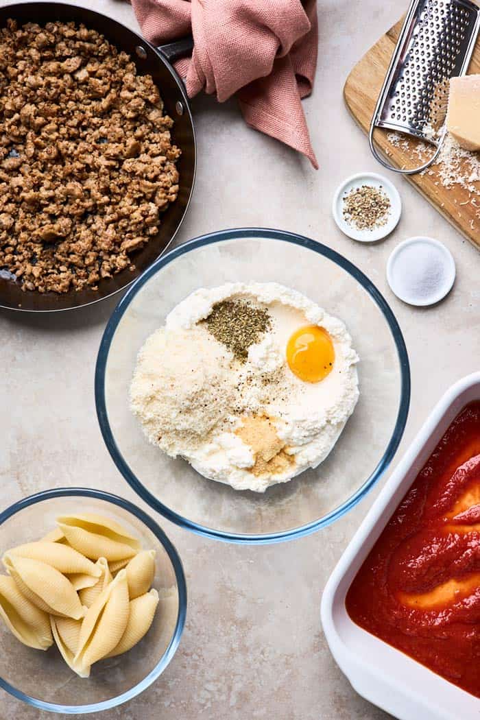 Filling ingredients in a glass bowl with cooked sausage and cooked pasta shells ready to assemble stuffed shells with meat