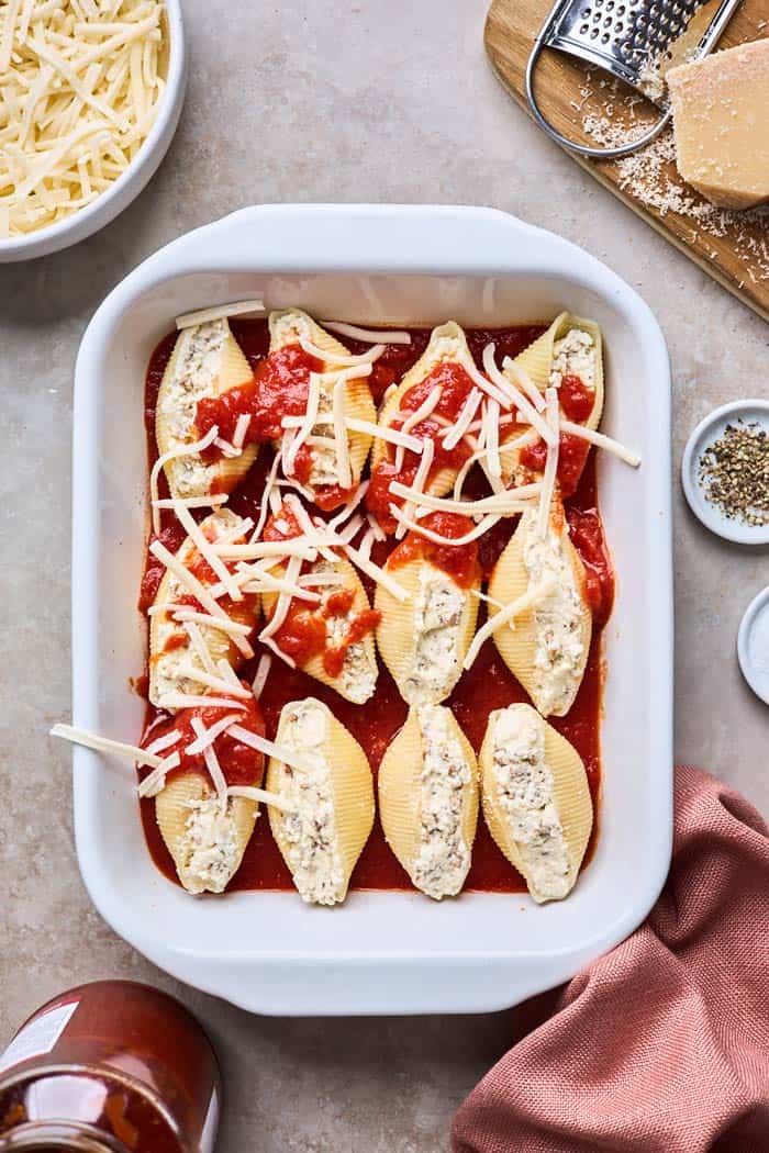 A filled casserole dish with stuffed shells and cheese and sauce layering it before baking
