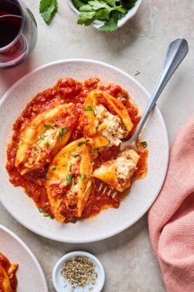 Three stuffed shells on a white plate with a fork eating out of one