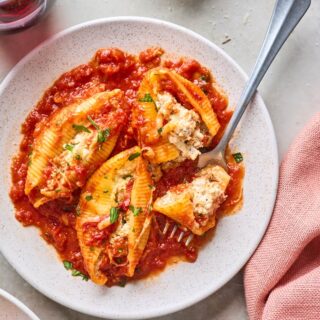 Three stuffed shells on a white plate with a fork eating out of one