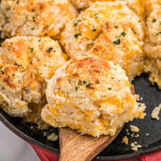 a cheddar bay biscuit being lifted from a pan with other biscuits