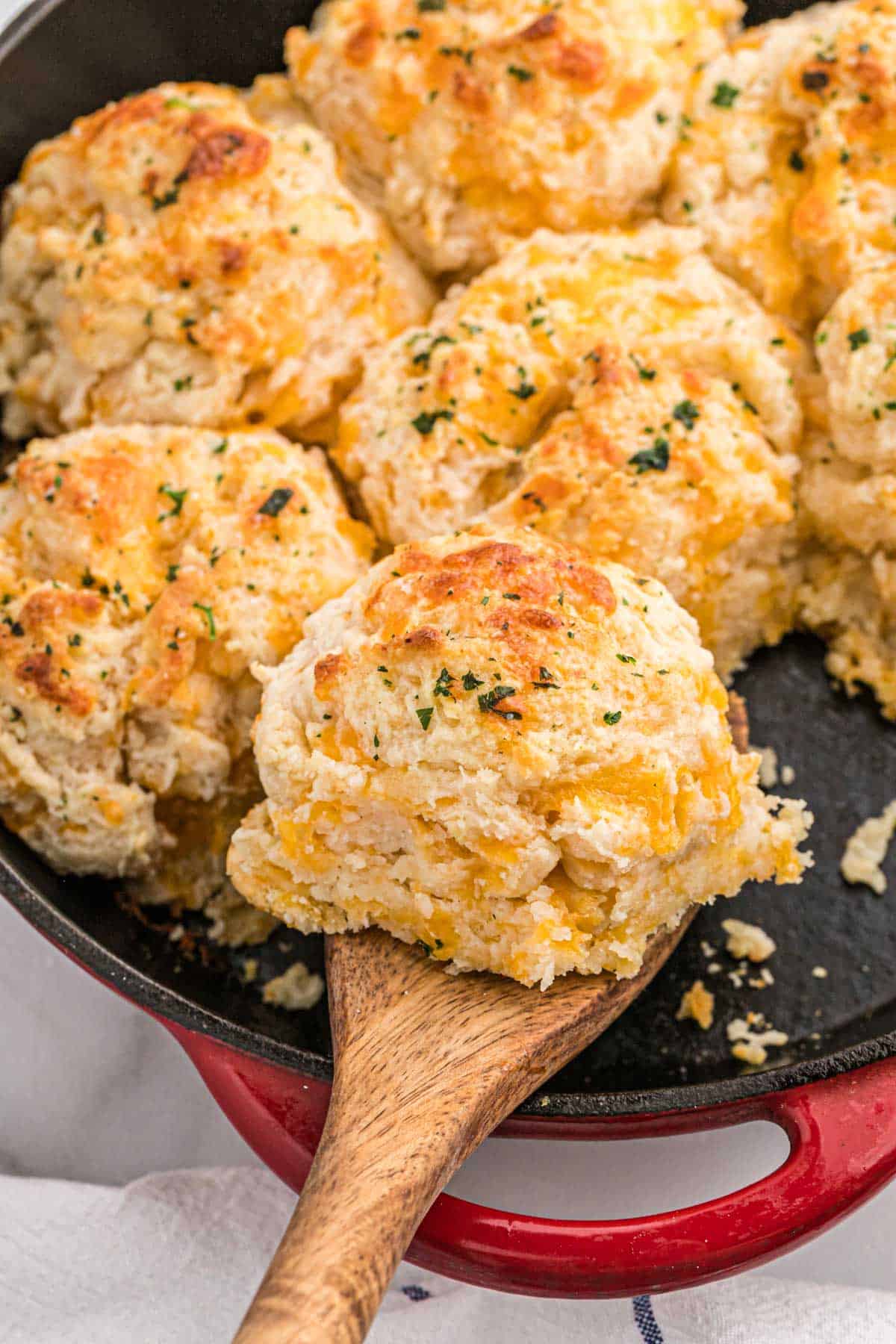 a cheddar bay biscuit being lifted from a pan with other biscuits