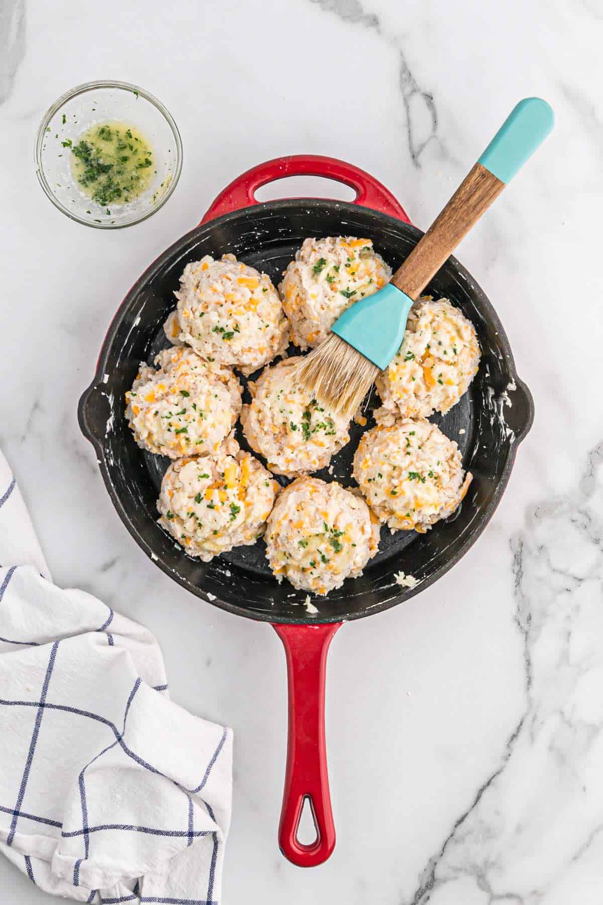 A pastry brush on top of the cheddar garlic biscuits in a cast iron pan.
