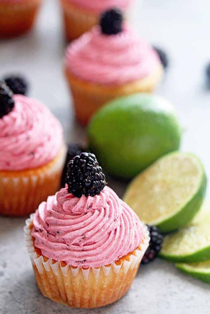 Blackberry limeade cupcakes topped with a single blackberry and limes decorating the scene