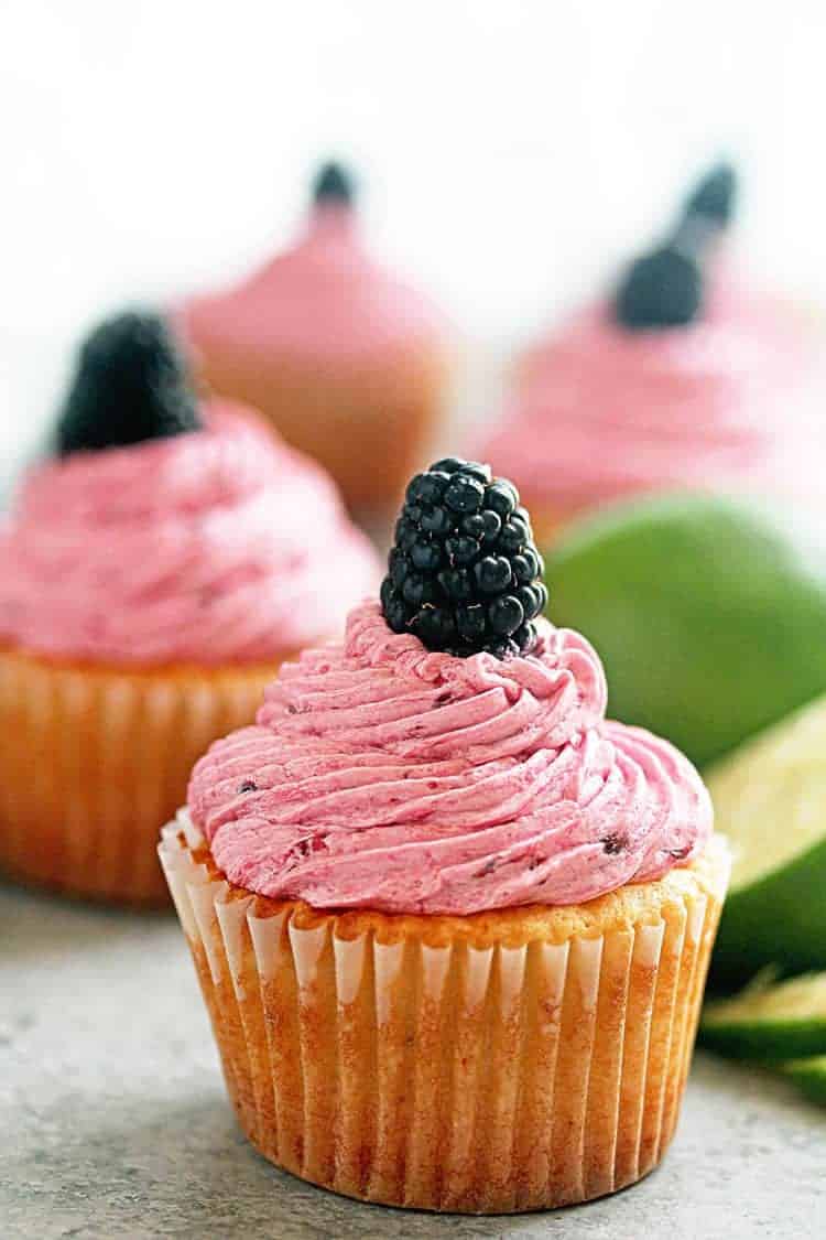 Close up of a blackberry lime cupcake topped with blackberry buttercream and one fresh blackberry.