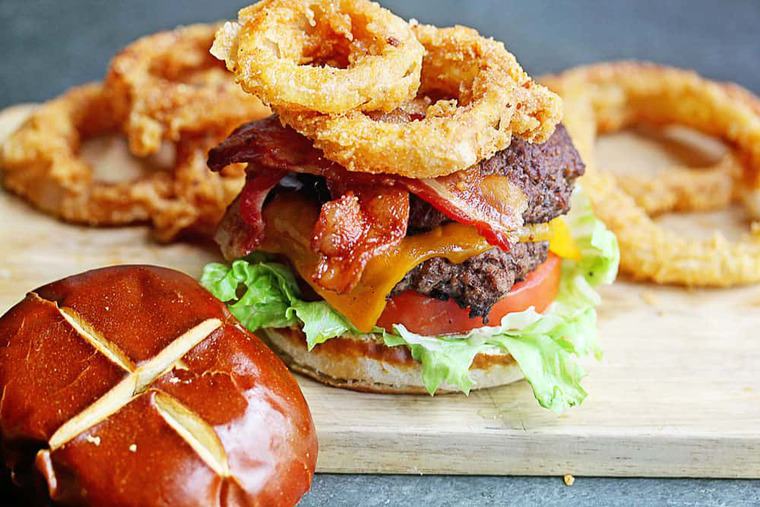 A delicious burger on pretzel bun with fried onion rings, bacon and melted cheddar