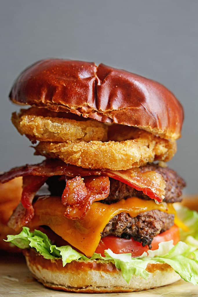 Close up of a ready to devour cheddar bacon burger with onion rings in the background