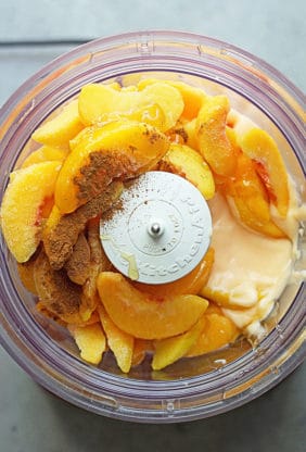 Frozen peaches, spices, sugar and yogurt in food processor ready to make fro yo recipe