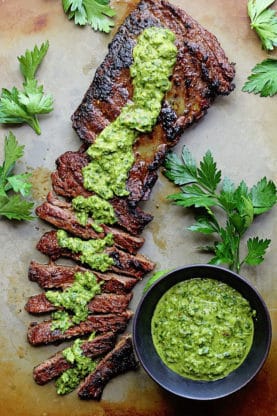 Overhead shot of Marinated Skirt Steak with Chimichurri drizzled all over it and a bowl of it next to it
