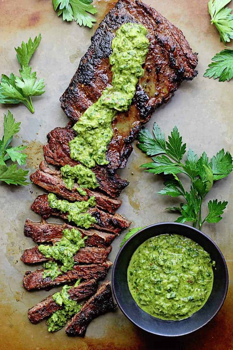 Overhead shot of a skirt steak topped with chimichurri sauce after being marinated with a flank steak marinade surrounded by cilantro.