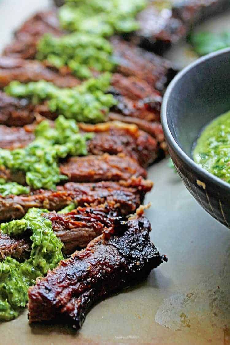 Close up of thinly sliced skirt steak topped with chimichurri sauce