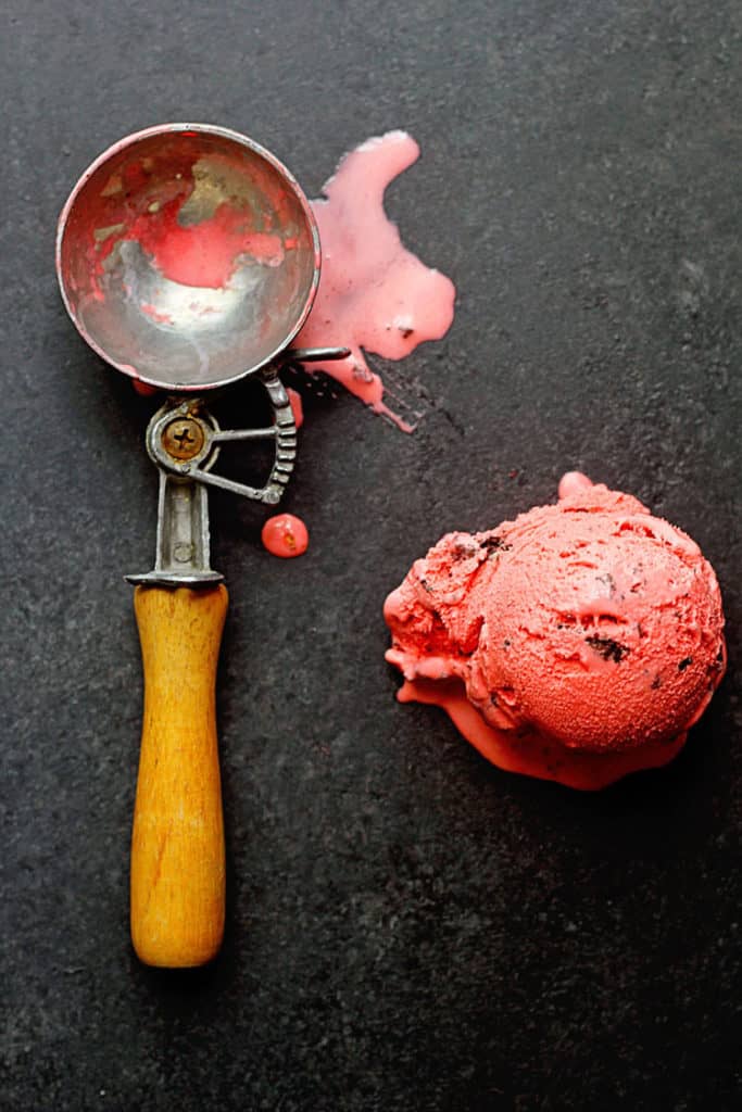 Red Velvet Ice Cream Recipe shown as a one scoop of it sits next to an ice cream scoop.
