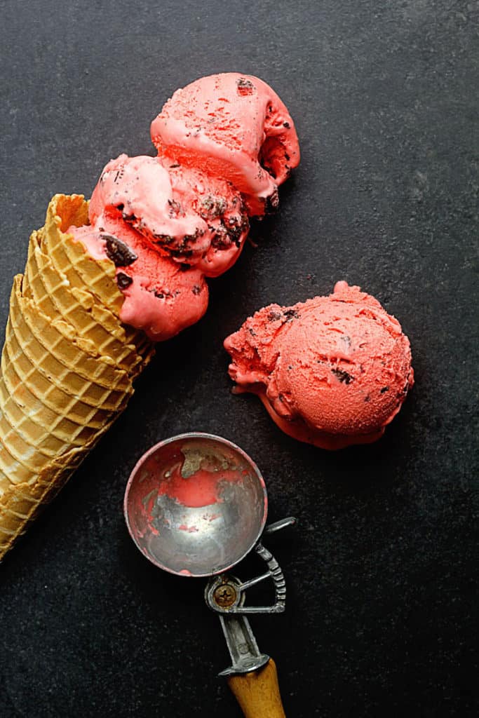 Oreo Red Velvet Ice Cream Recipe displayed with three scoops in a waffle cone and one scoop on the side next to it.