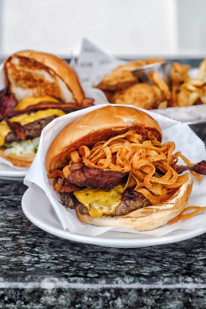 Two cheeseburgers wrapped in white paper on white plates from Strip Burger on the Las Vegas strip