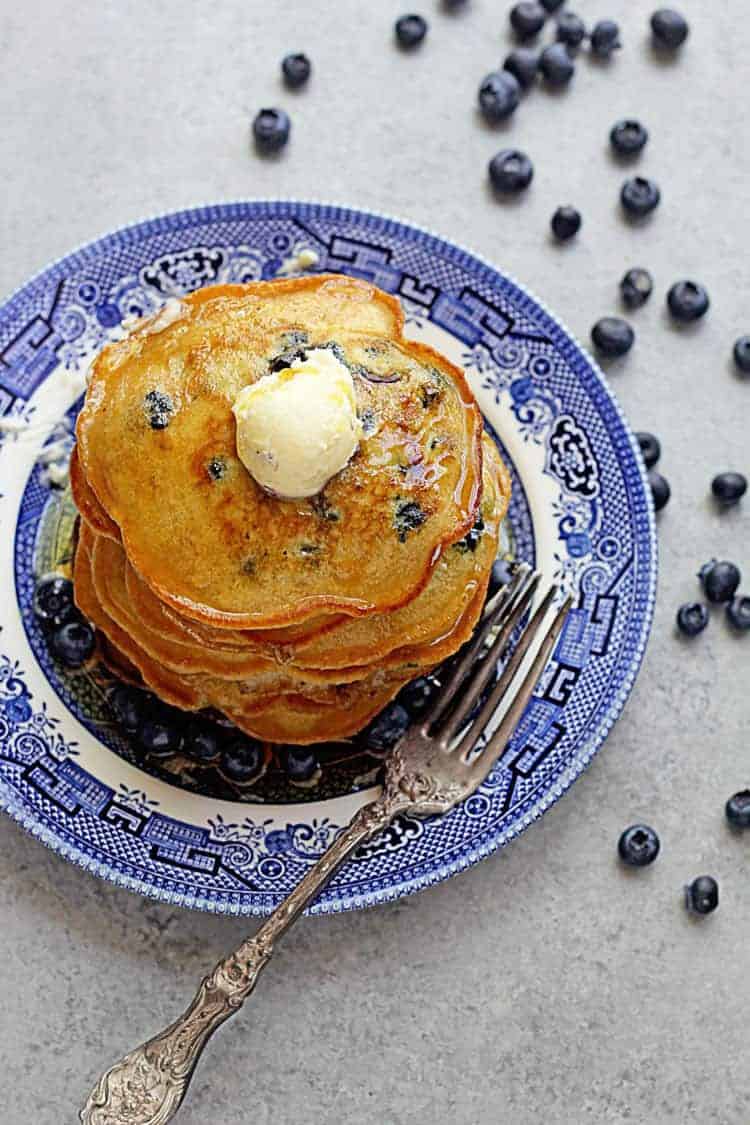 Overhead shot of this Blueberry Pancake Recipe topped with syrup and butter and surrounded by fresh blueberries.