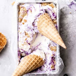 Overhead shot of blueberry ice cream with two waffle cones against gray background