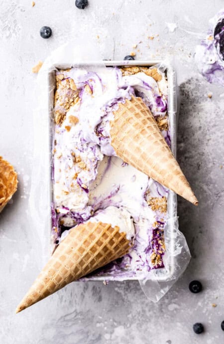 Overhead shot of blueberry ice cream with two waffle cones against gray background