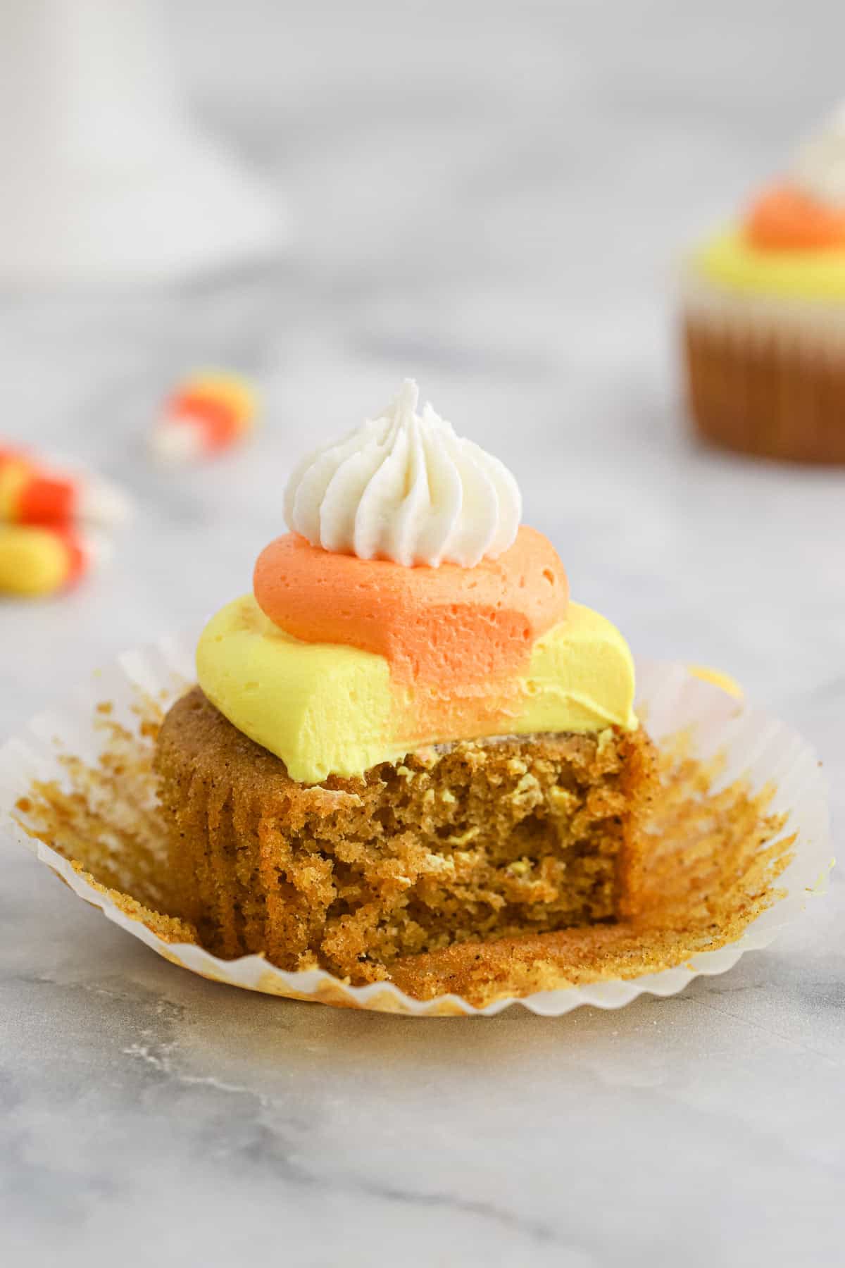 Several Pumpkin Cupcakes with Candy Corn Buttercream with candy corn pieces and small plastic pumpkins decorating the scene