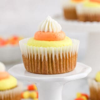 Pumpkin cupcake with candy corn frosting on a cake stand with more in back.