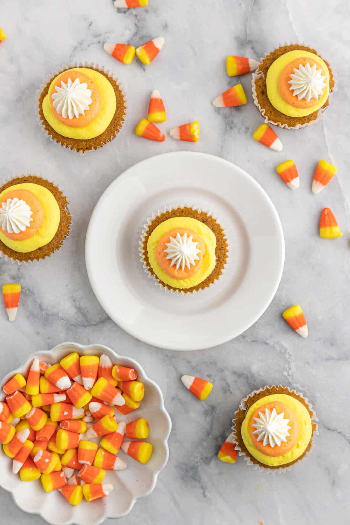 Pumpkin Cupcakes with Candy Corn Buttercream on white plates with candy corn scattered