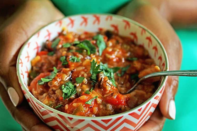 Hands holding a cup full of Jambalaya Soup with a spoon in it