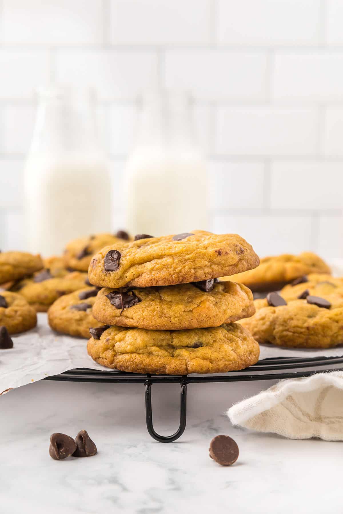 Pumpkin chocolate chip cookies on the table with three stacked on top of each other in front of more on a wire rack.