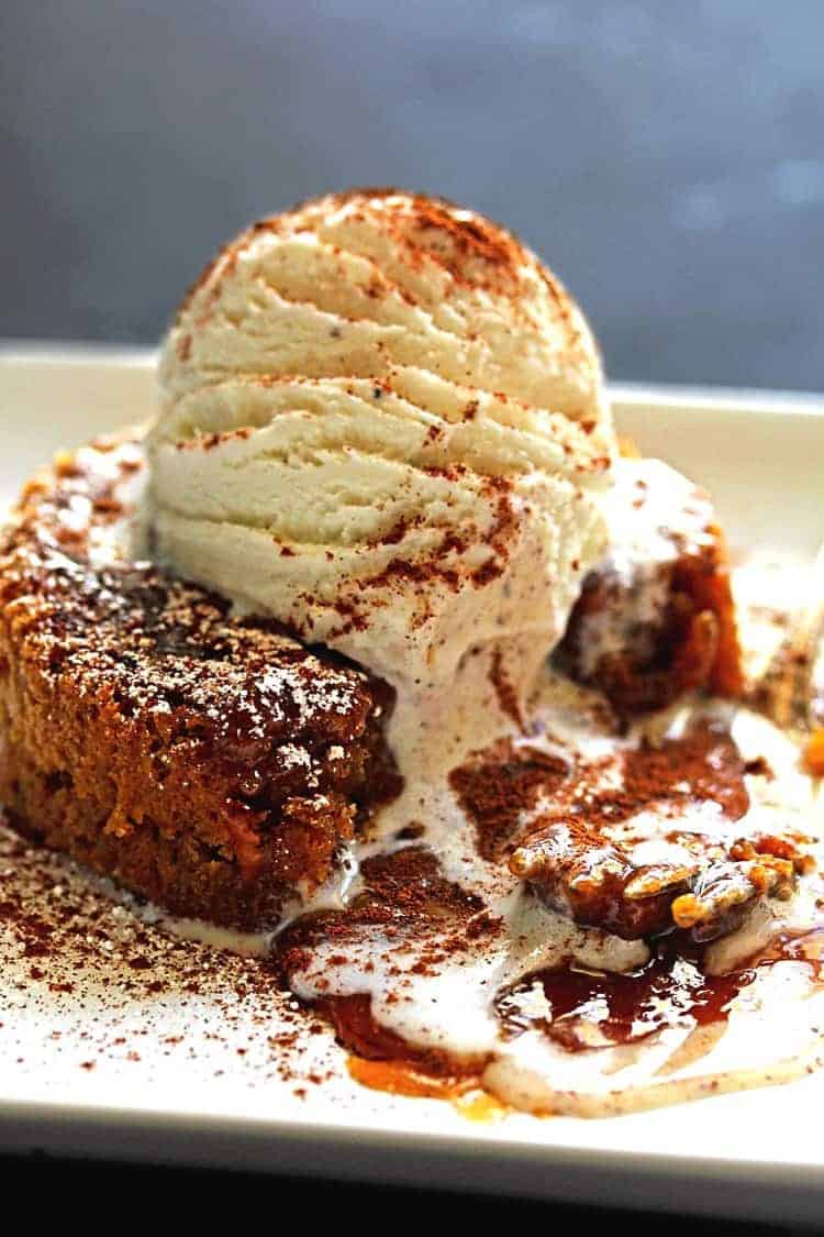 A delicious pumpkin caramel lava cake recipe oozing with melted caramel and topped with vanilla ice cream is being served with fork on white plate