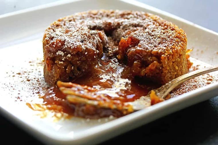 A caramel lava cake oozing caramel ready to serve on a white plate with a fork