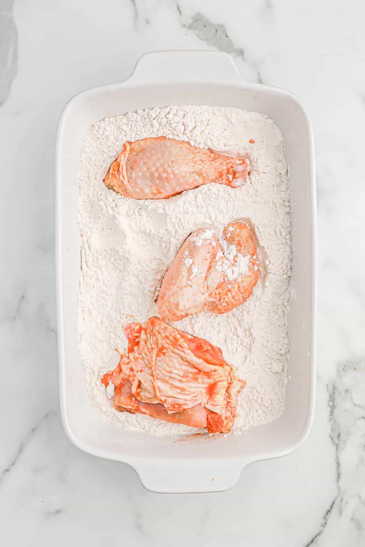 Brined chicken pieces in a dish with flour mixture.