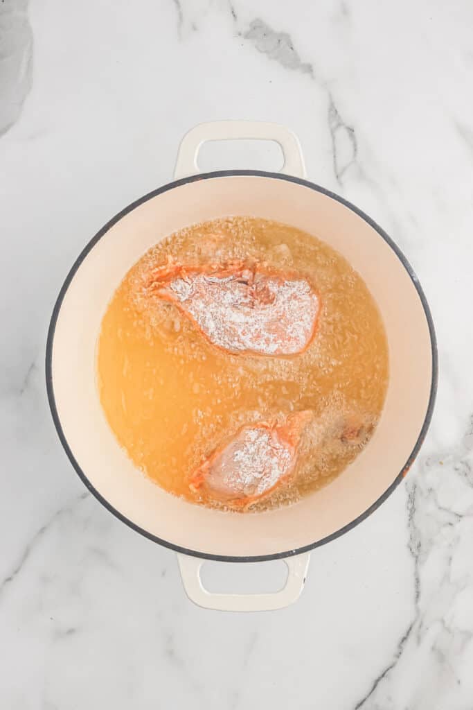 Buttermilk fried chicken cooking in oil in a large pot.