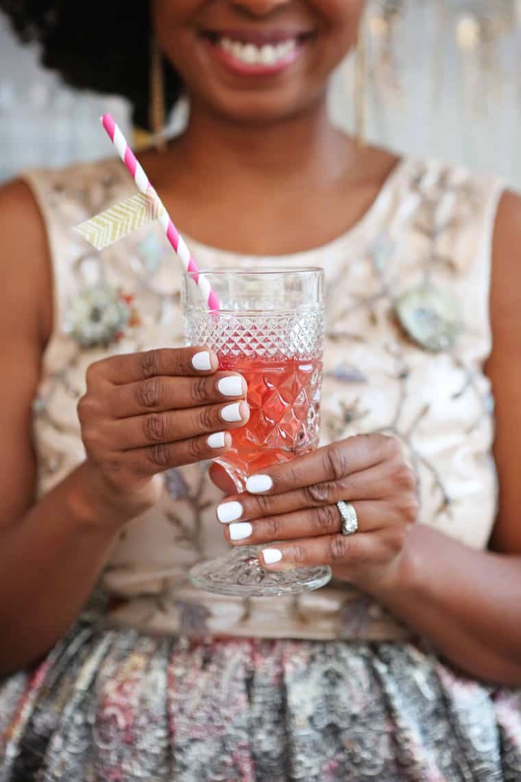 Jocelyn Delk Adams holding a bubbly cocktail with a white and pink striped straw in it