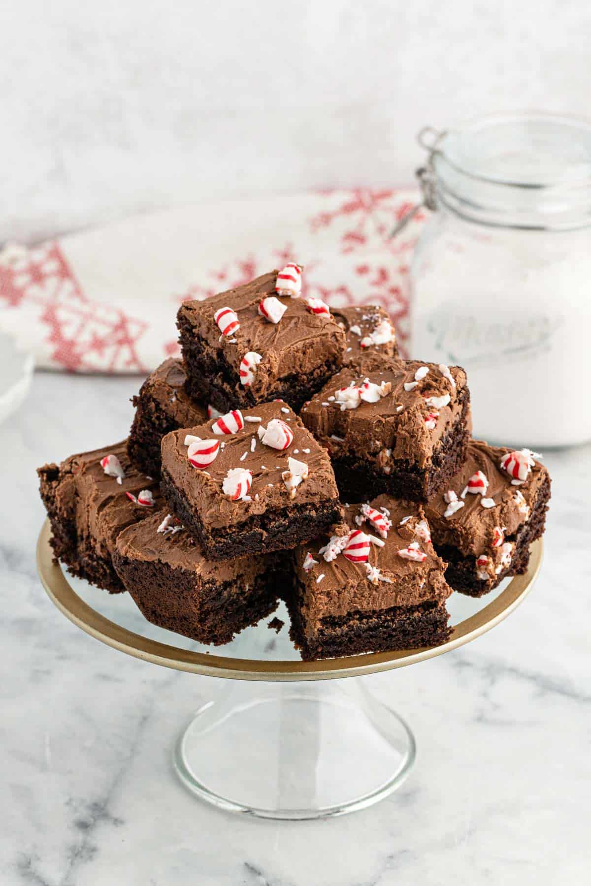 A platter of peppermint brownies on the table with a jar of sugar behind it and a white and red napkin.