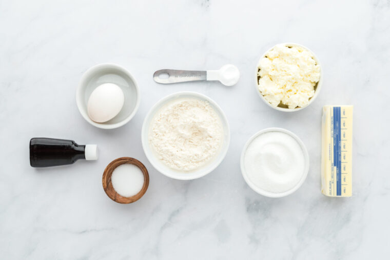 Flour, sugar, ricotta, egg and other ingredients to make ricotta cheese cookies on white countertop