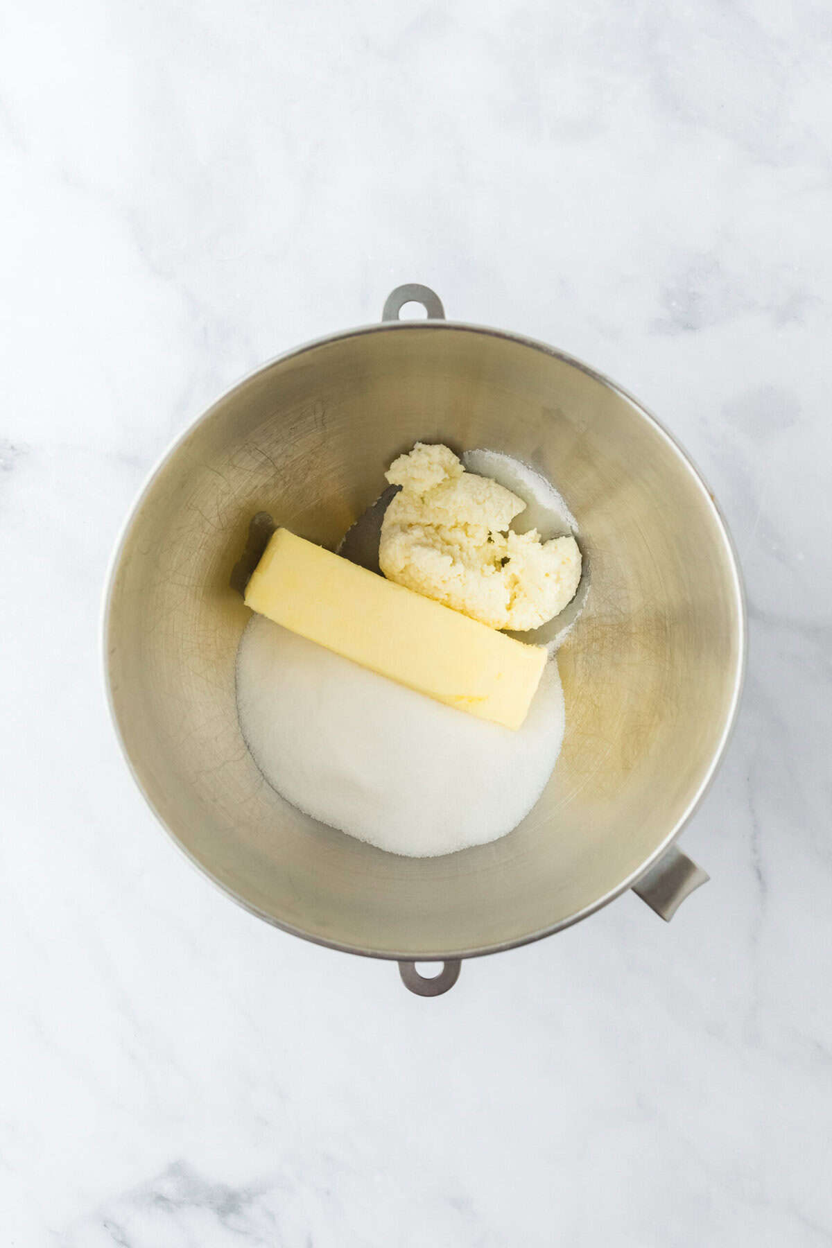 Butter, ricotta cheese and granulated sugar in a stand mixer bowl on white background