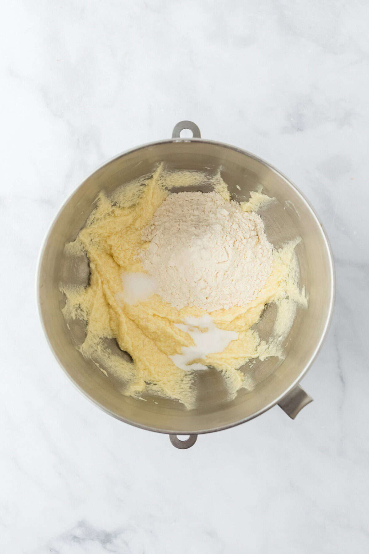 Dry ingredients added to a stand mixer bowl on white background