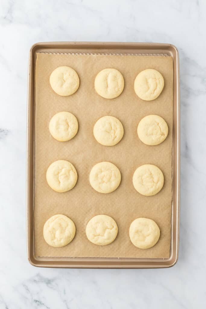 Baked ricotta cookies on a parchment lined baking sheet on white countertop
