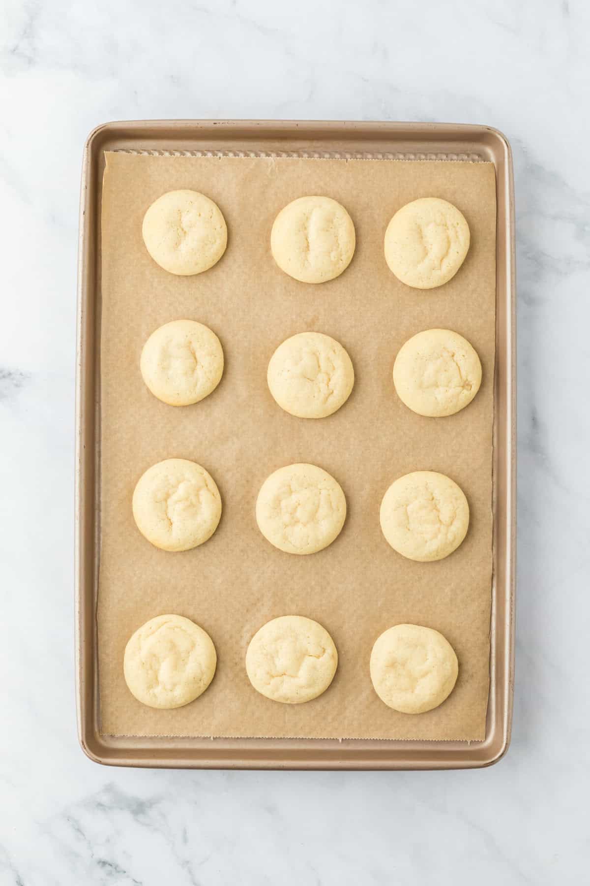 Baked ricotta cookies on a parchment lined baking sheet on white countertop