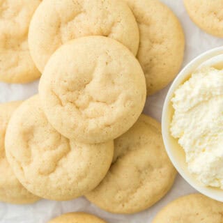 Ricotta cookies overhead stacked on each other next to a bowl of ricotta on a white countertop