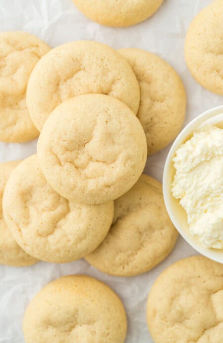 Ricotta cookies overhead stacked on each other next to a bowl of ricotta on a white countertop