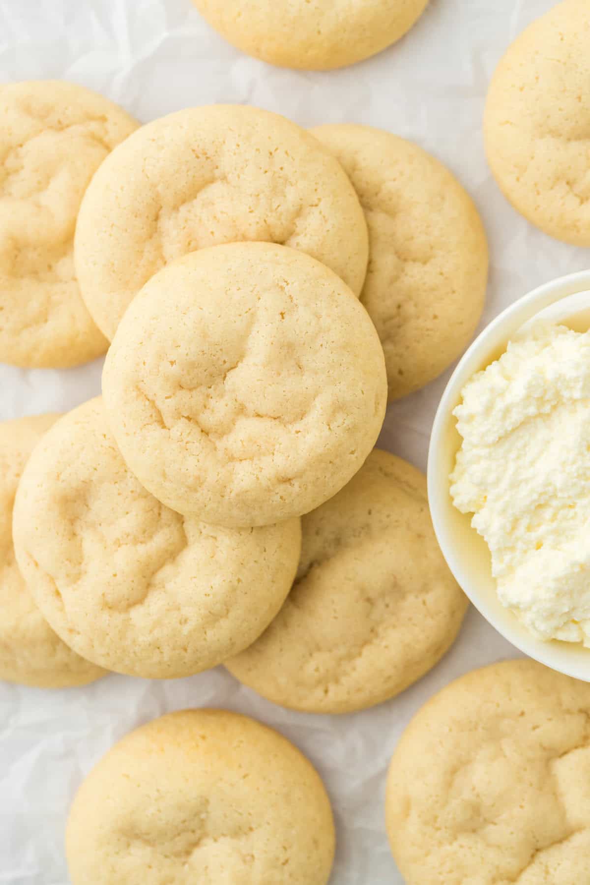 Ricotta cookies overhead stacked on each other next to a bowl of ricotta on a white countertop