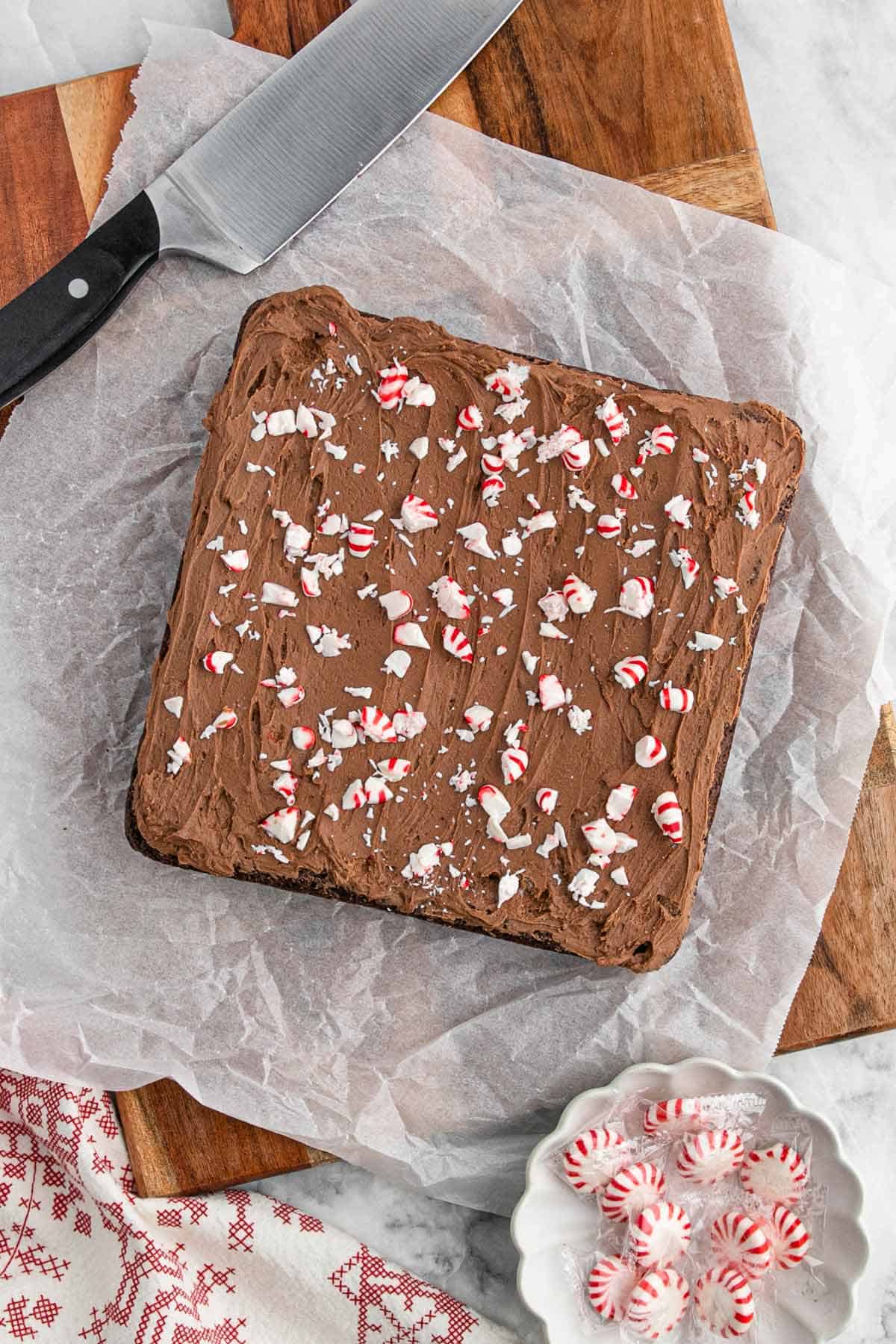 Peppermint brownies with frosting and peppermints on top on parchment ready to cut into pieces.