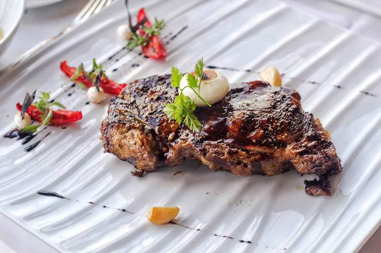 Grilled steak being served on a square, white plate