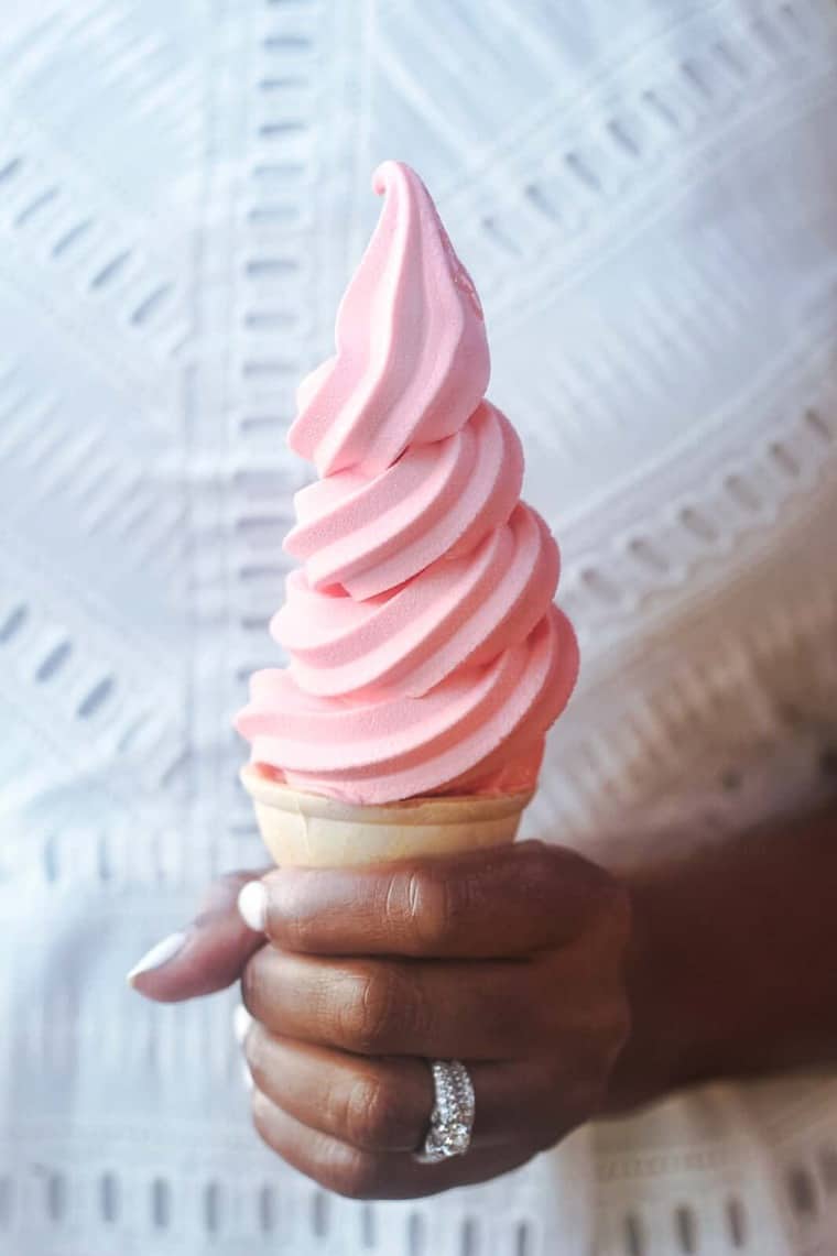 Soft serve strawberry ice cream on a cone being held by Jocelyn Delk Adams